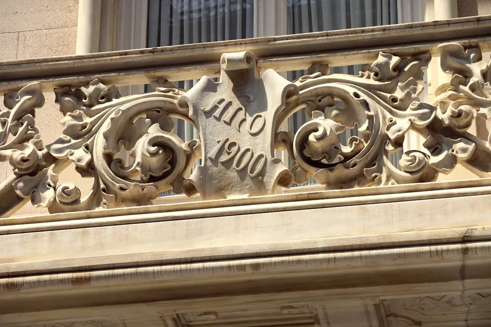 Balcón de piedra tallada con la fecha 1900 en un edificio modernista de la Calle Mayor